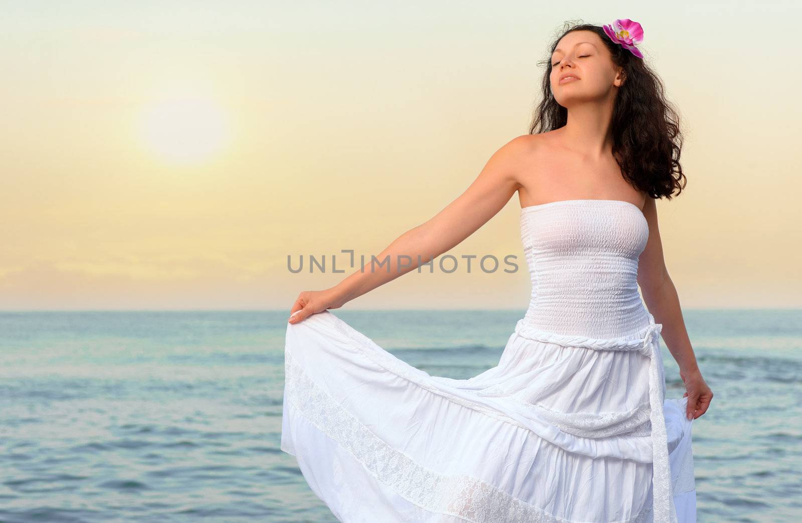 The woman in a white sundress on seacoast. Sunset illumination