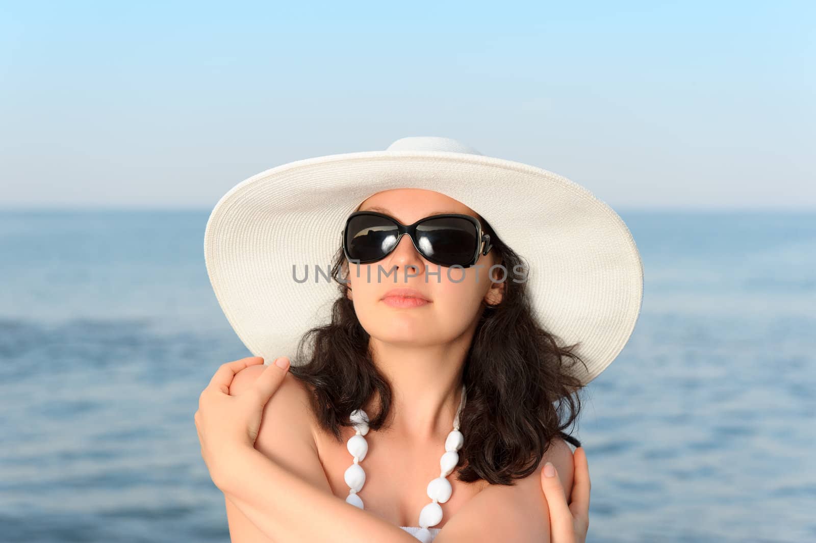 The woman on seacoast. In sun glasses, a sundress, a hat.