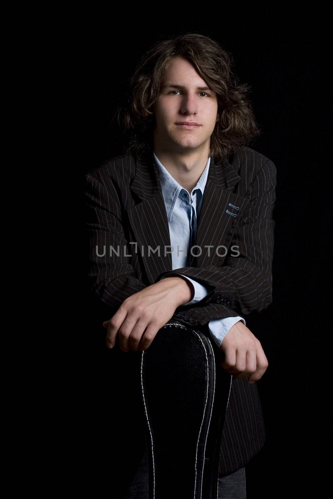  portrait of a male teenager wearing a suit leaning on a instrument case