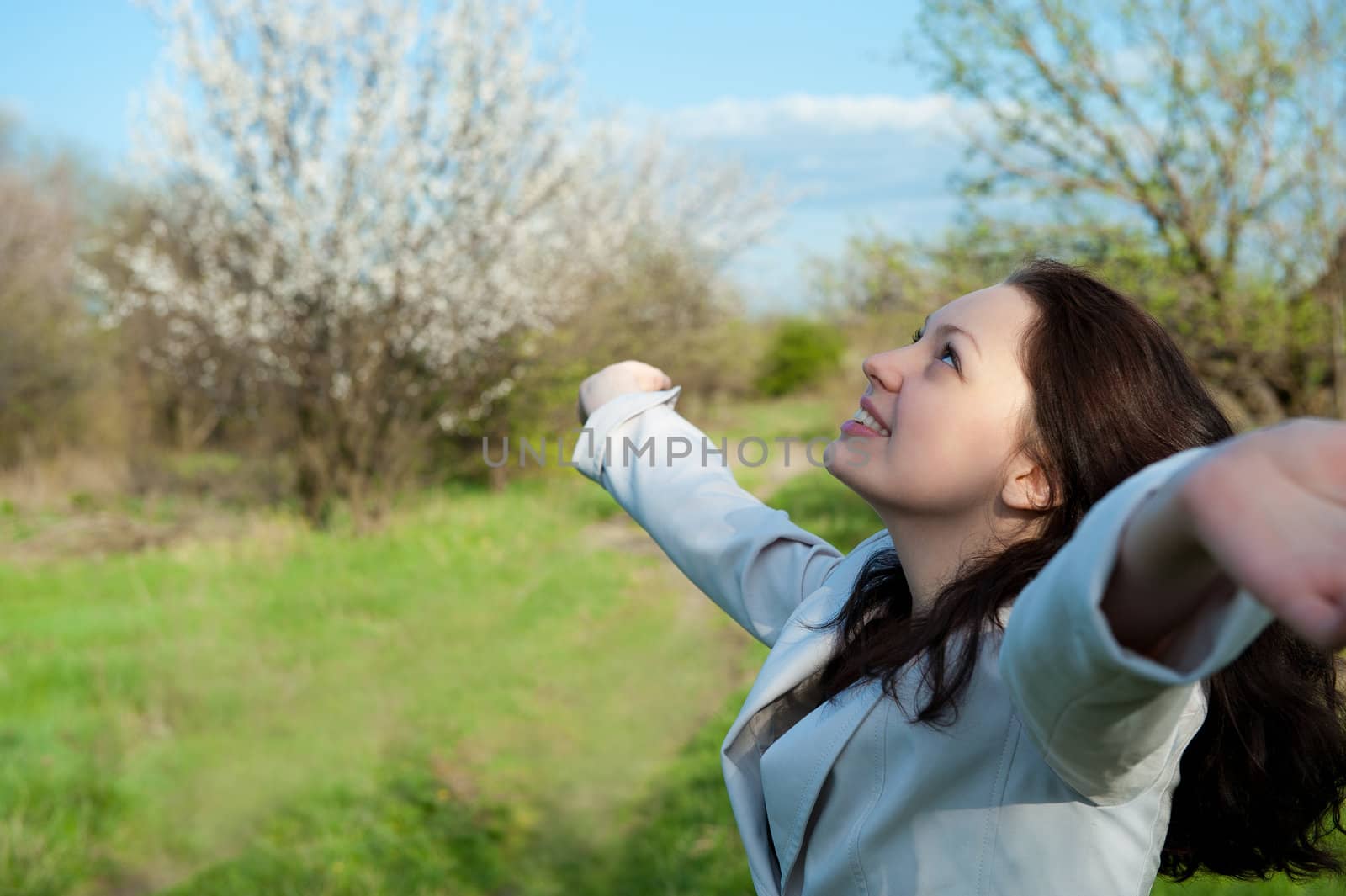 The happy attractive woman with the lifted hands. Against the spring nature