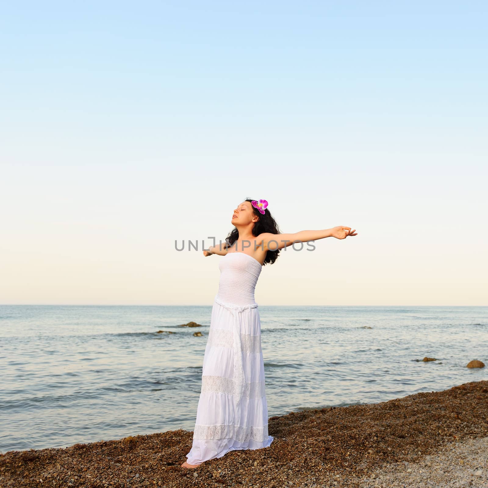 The woman in a white sundress on seacoast with open hands. A picturesque landscape