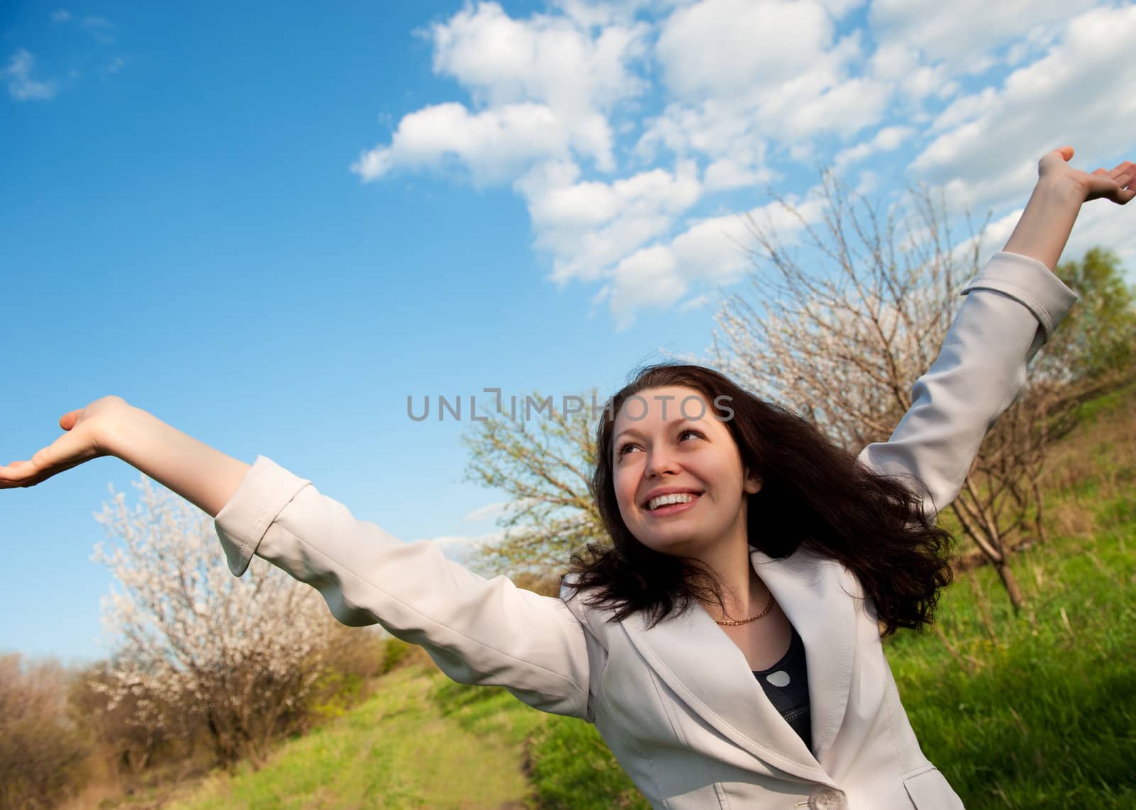 The happy attractive woman with the lifted hands. Against the spring nature