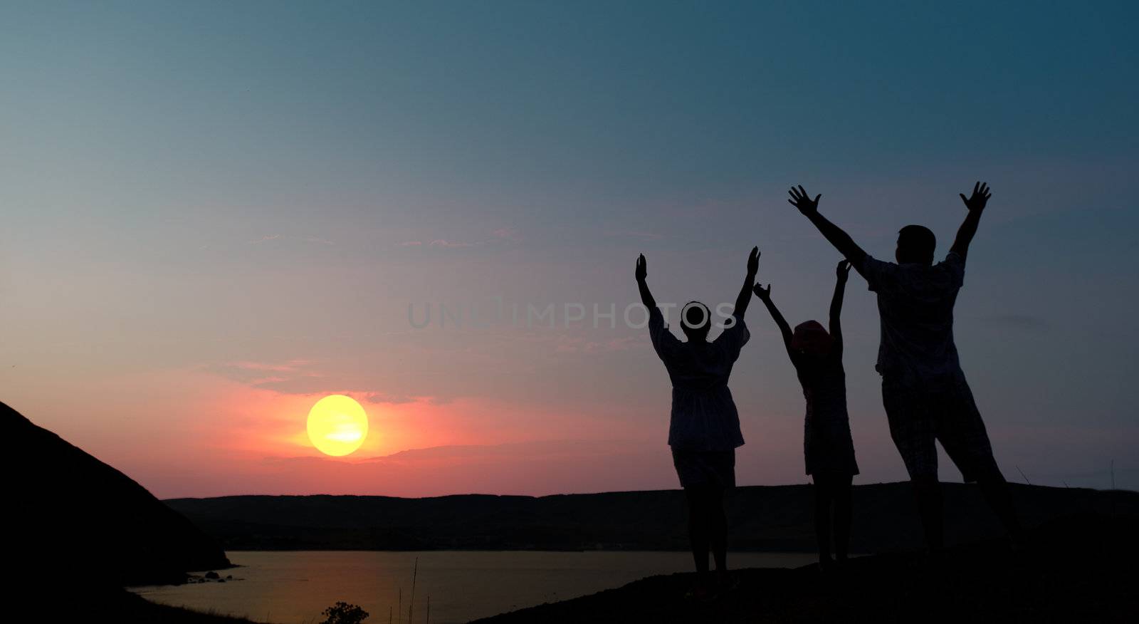 The family from three persons welcomes the sunset sun.