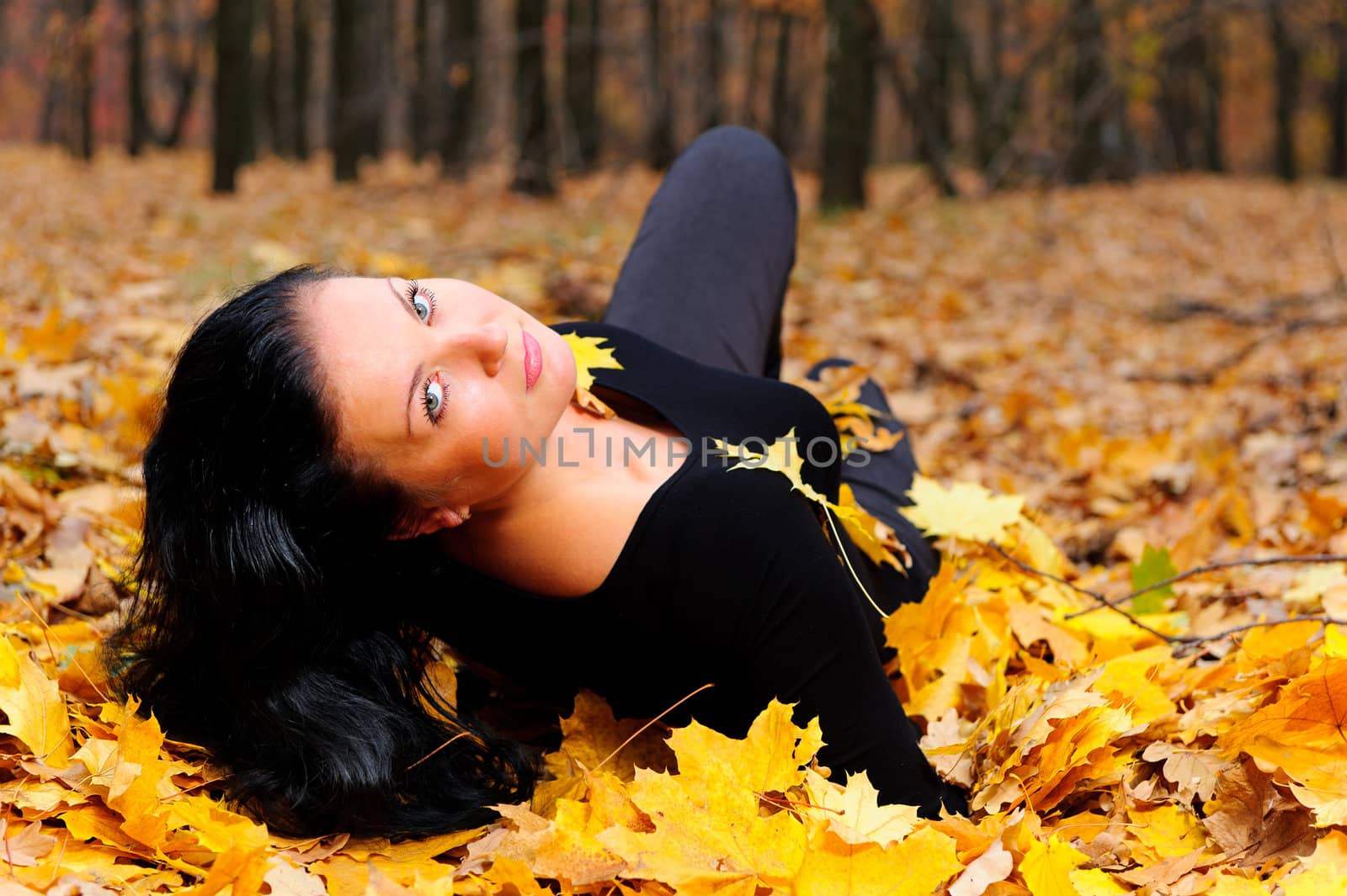 The attractive woman in autumn forest. Lies on yellow leaf