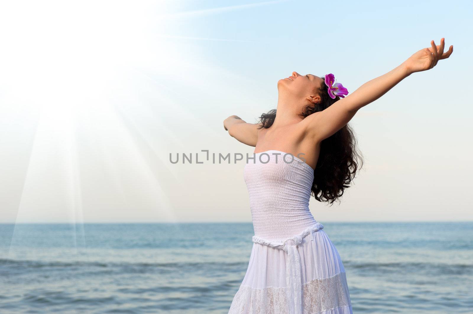 The woman in a white sundress on seacoast with open hands. Sun light