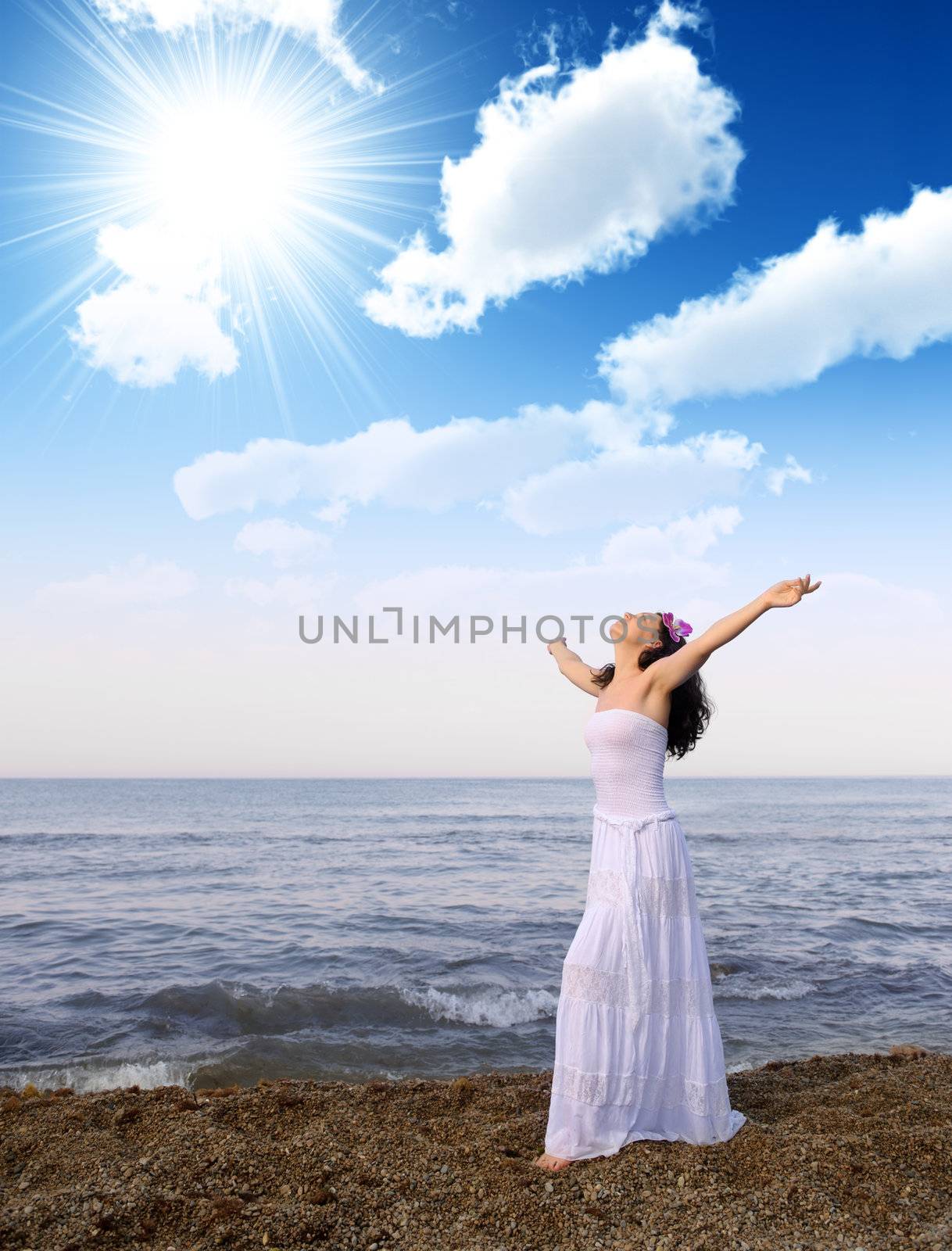 The woman in a white sundress on seacoast with open hands. Cloud sky