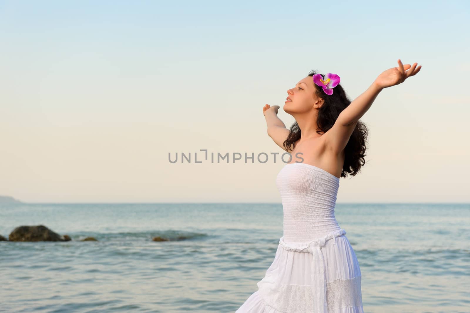 The woman in a white sundress on seacoast with open hands. A picturesque landscape