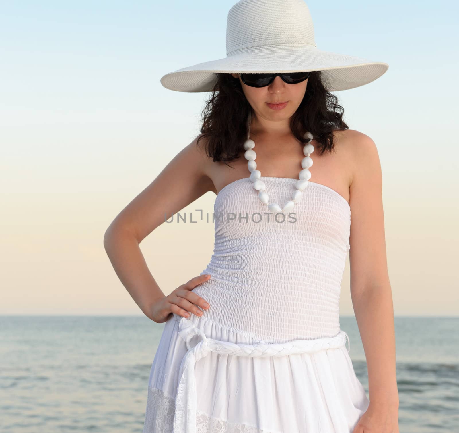 The woman on seacoast. In sun glasses, a sundress, a hat.