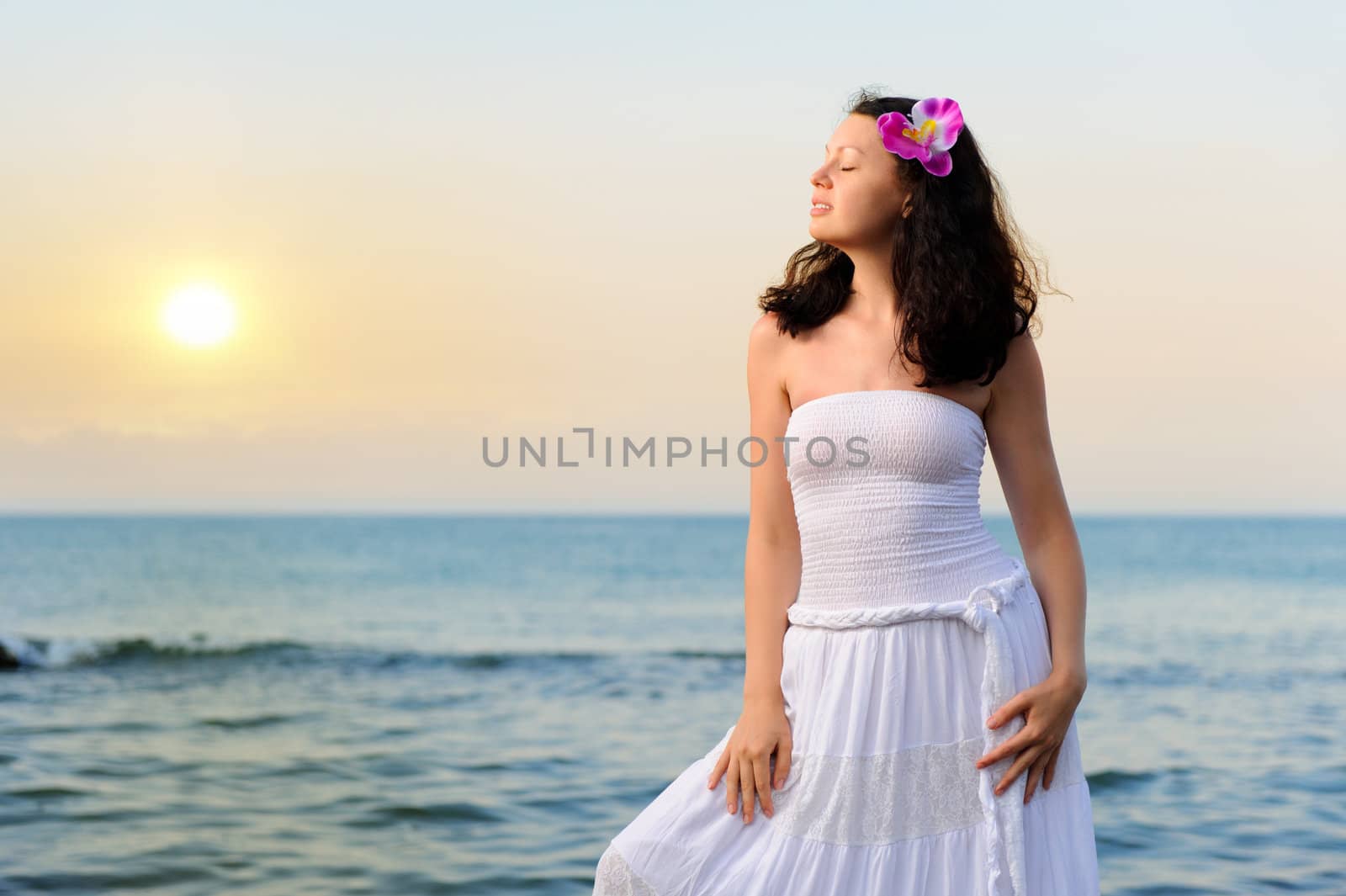 The woman in a white sundress on seacoast. Sunset illumination