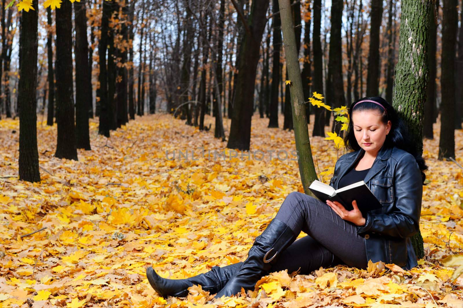 The attractive woman reads the book in autumn forest.