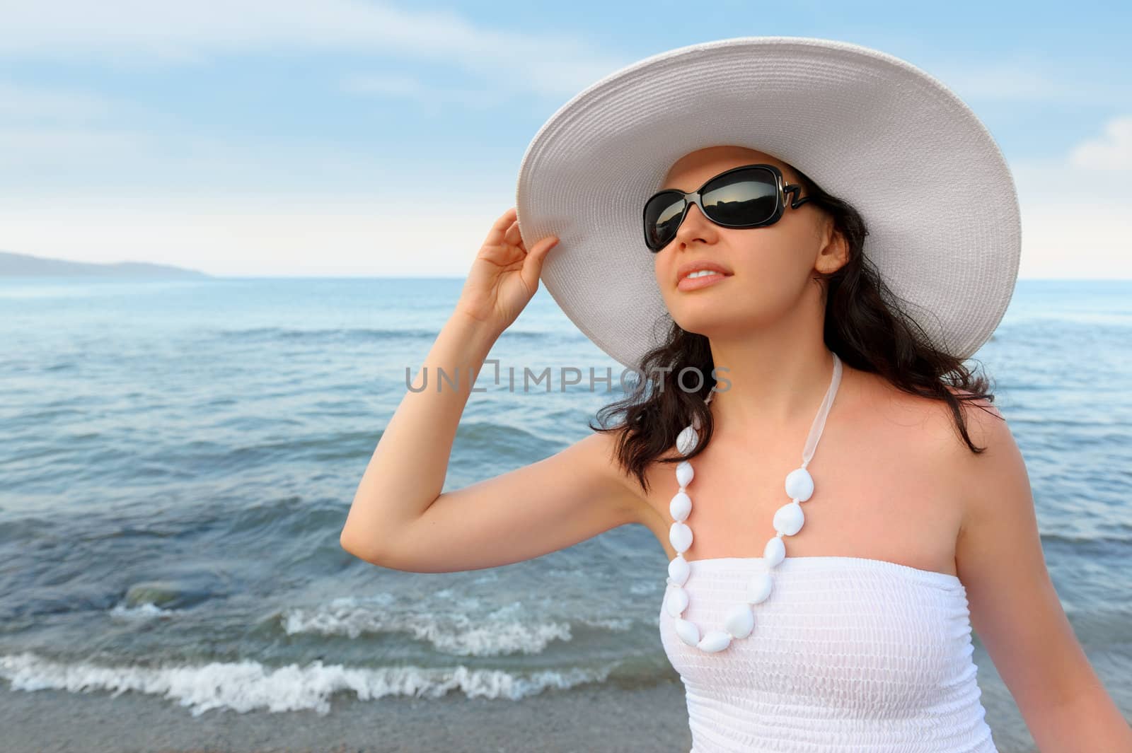 The woman on seacoast. In sun glasses, a sundress, a hat.