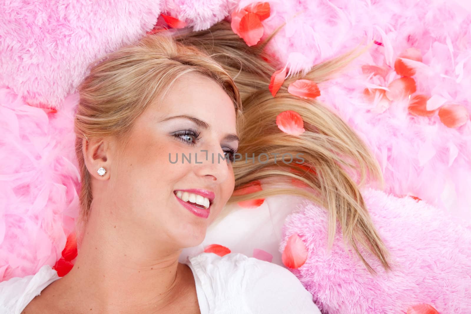 Beautiful blond girl lying on pink feathers and rose petals