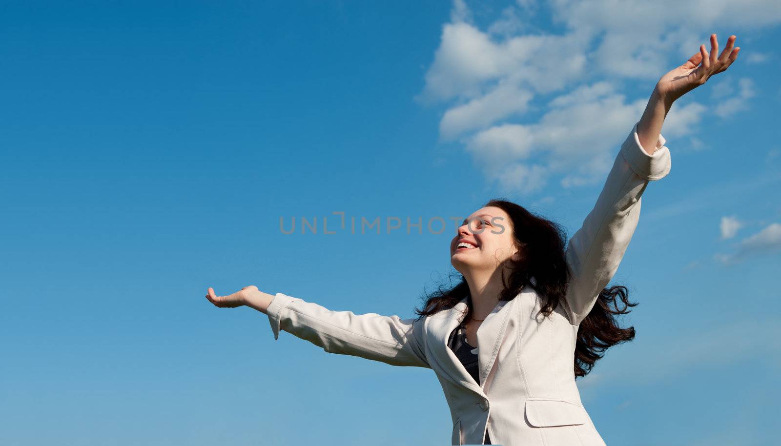 The happy attractive woman with the lifted hands. Against the blue sky