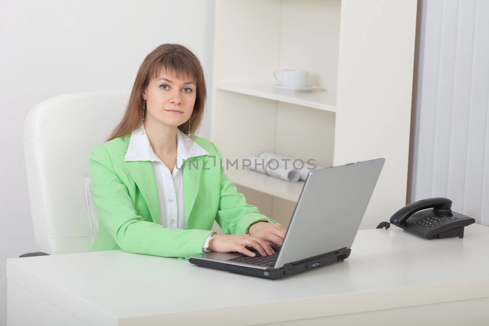 The young beautiful woman - the secretary sits on a workplace with the computer