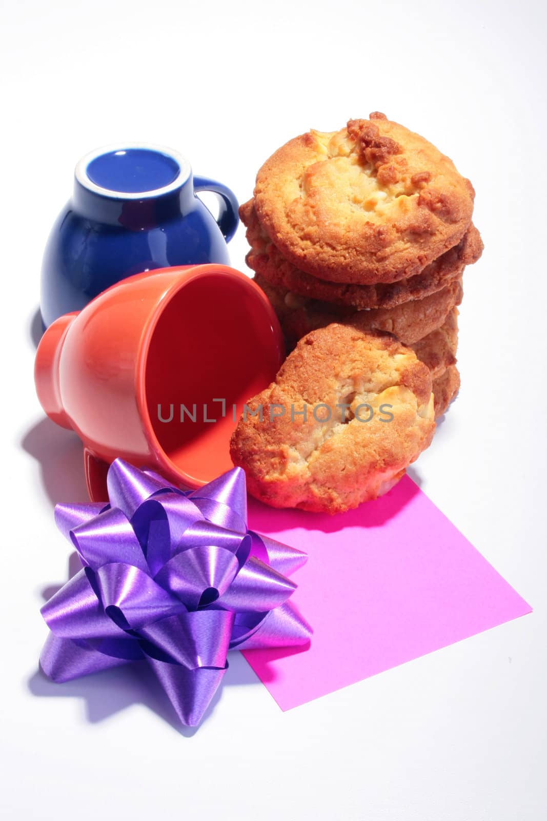 Sweet cookies with cups for coffee, a celebratory bow and a label of red colour in the foreground.