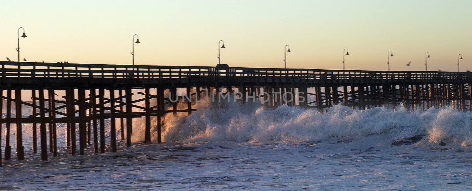 Ocean waves throughout at storm crashing into a wooden pier.