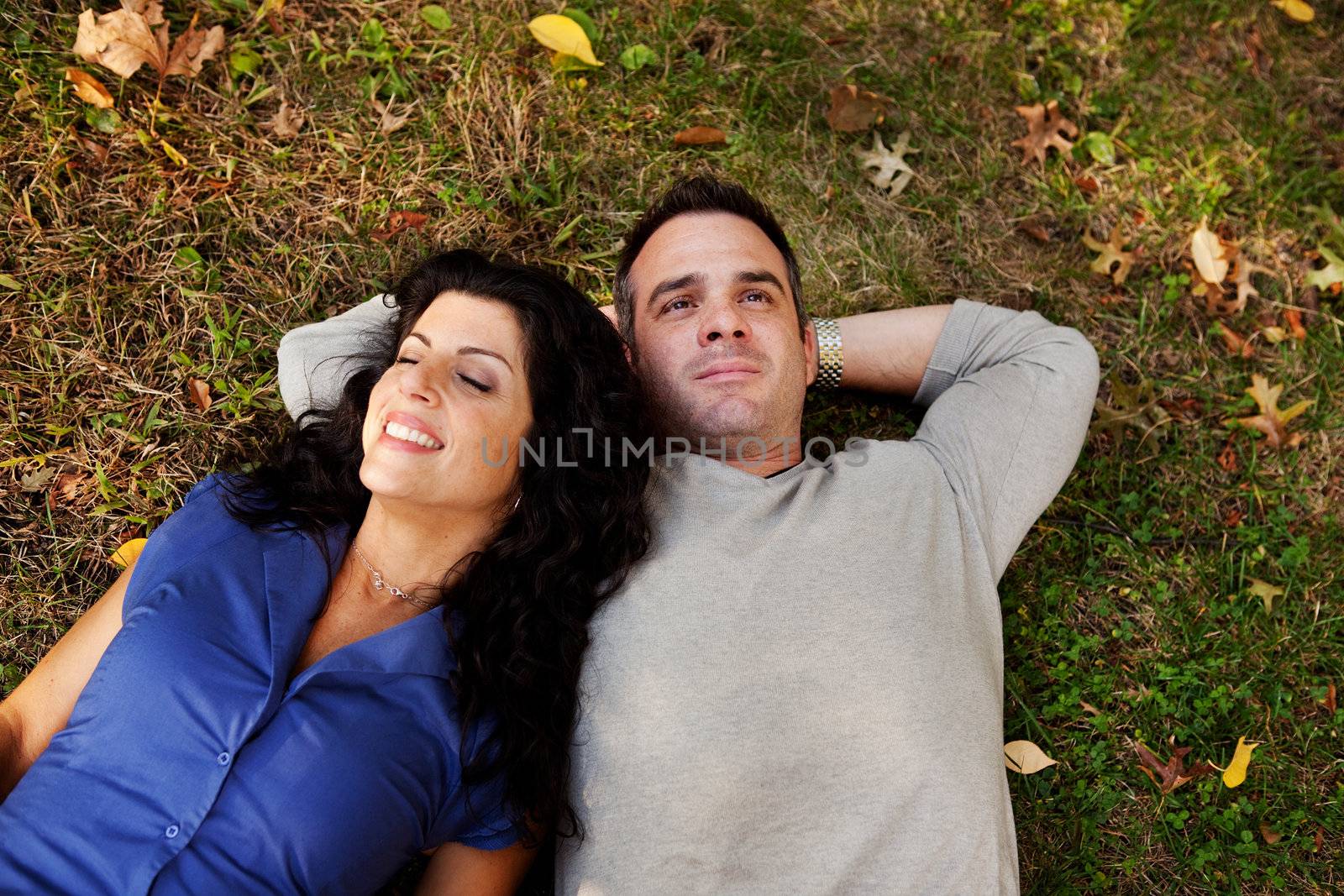 A couple laying on grass in a park daydreaming.  Focus on the womans eyes