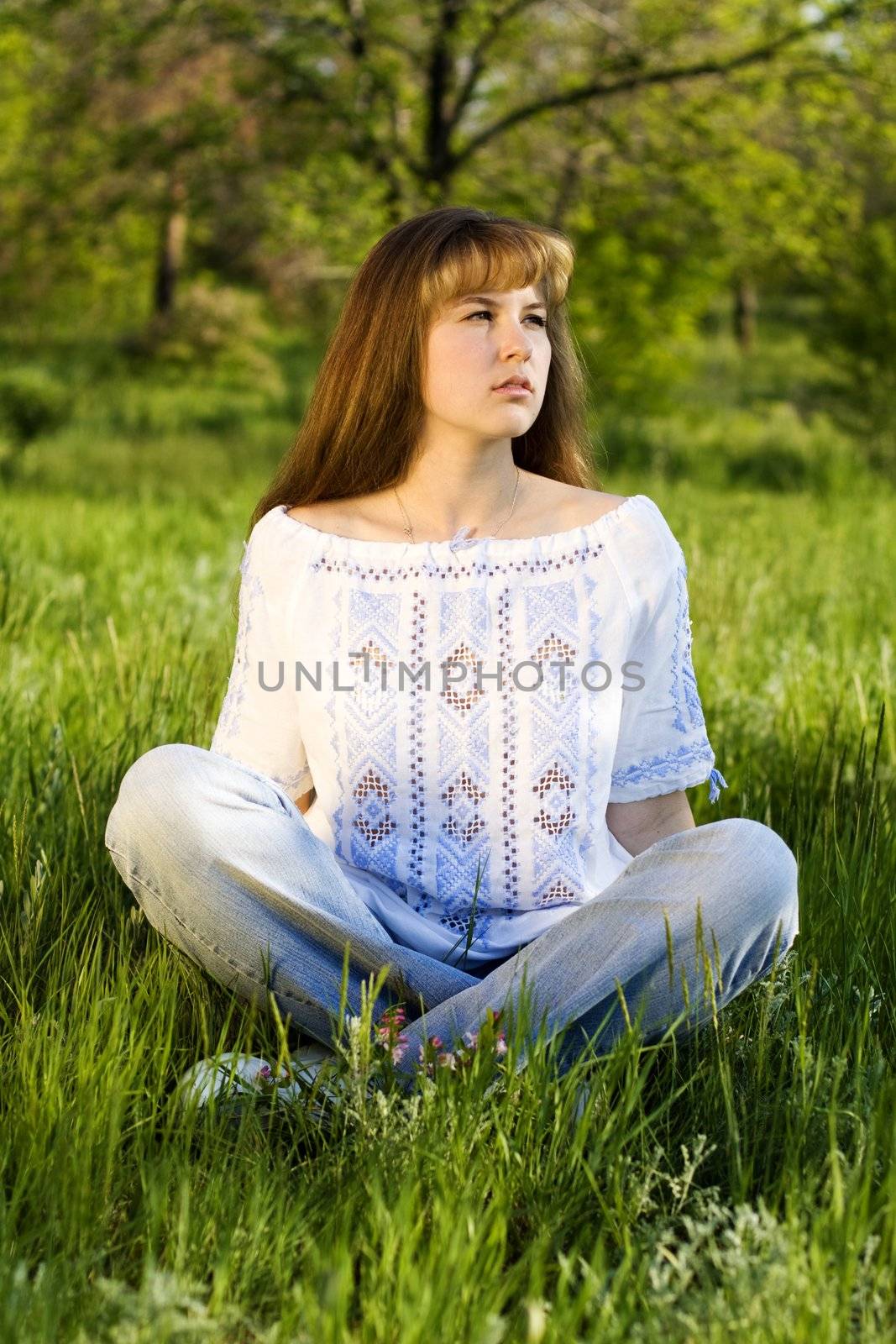 Young woman meditating outdoors, sitting on green grass