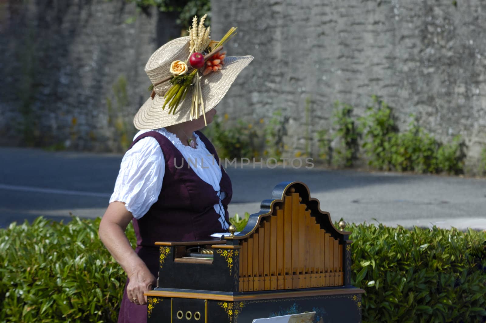 A woman barrel organ player, with a wonderfully summery hat, playing her music to an empty street.