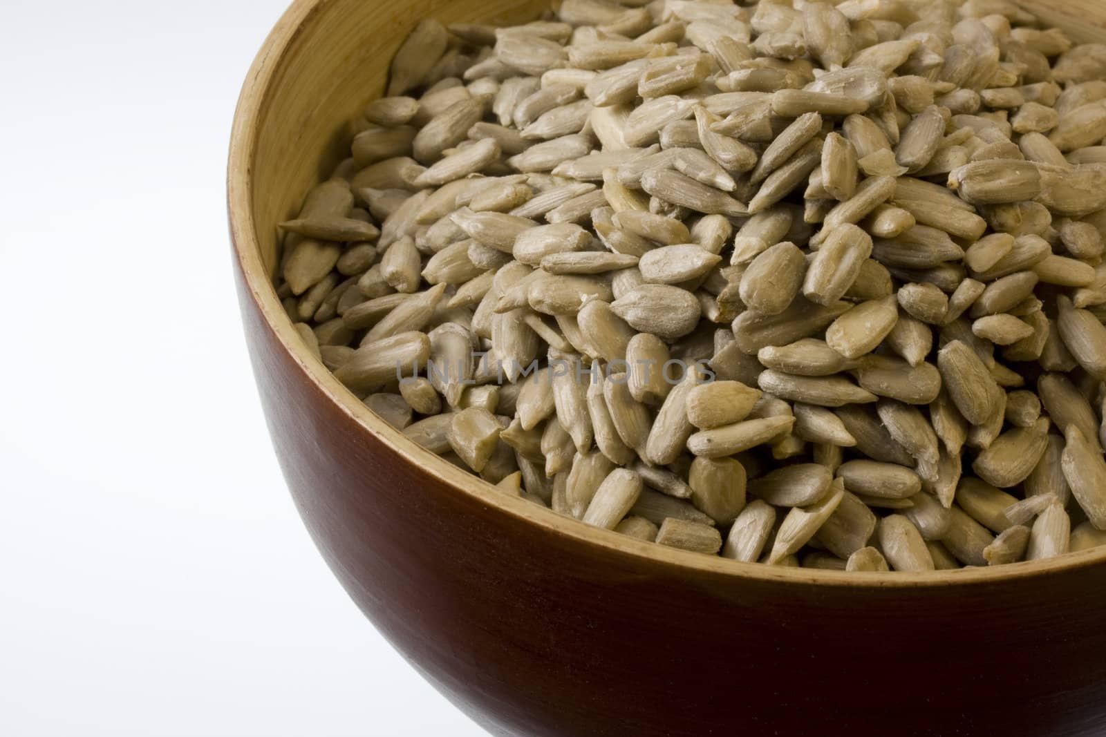 a wooden bowl of shelled sunflower seeds against white background, copy space
