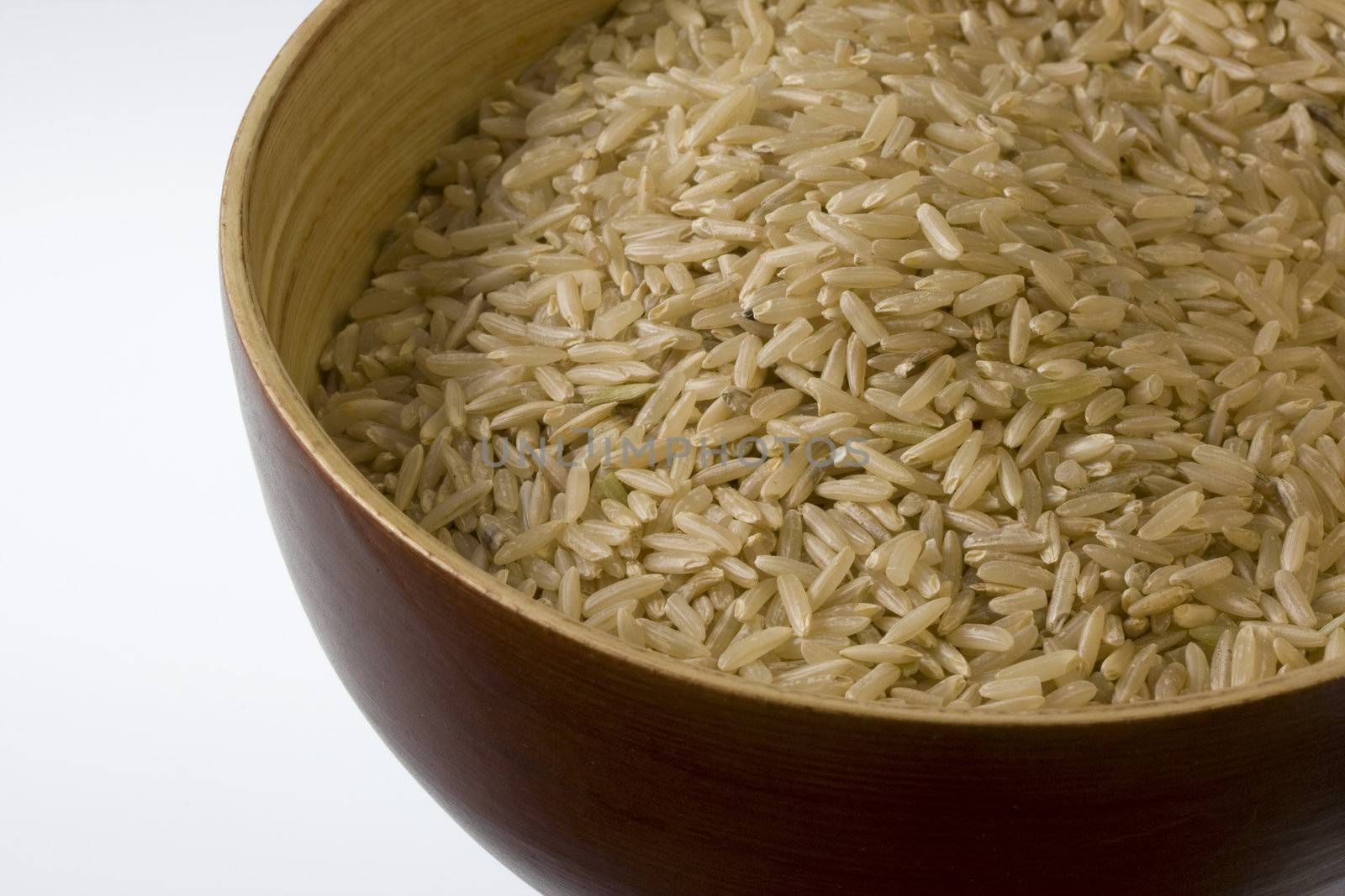a wooden bowl of long grained brown rice against white background