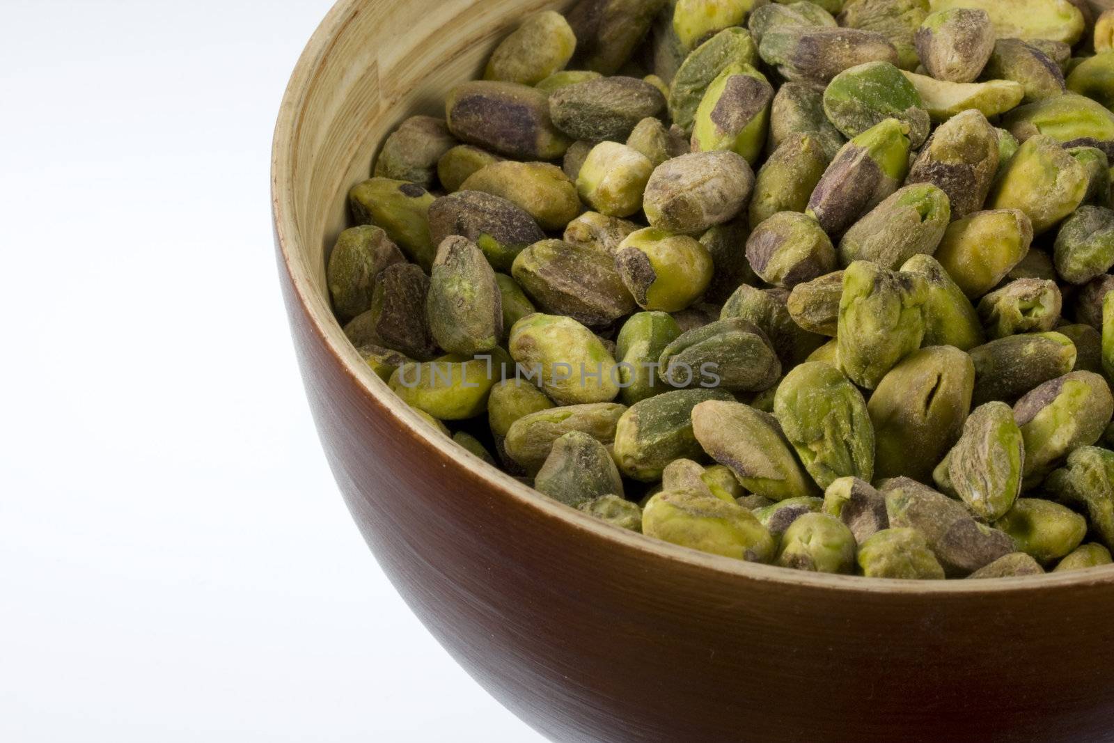 a wooden bowl of shelled pistachio nuts against white background