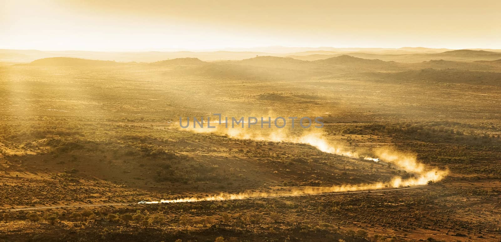 two cars leave plumes of dust as they go through the desert at sunset