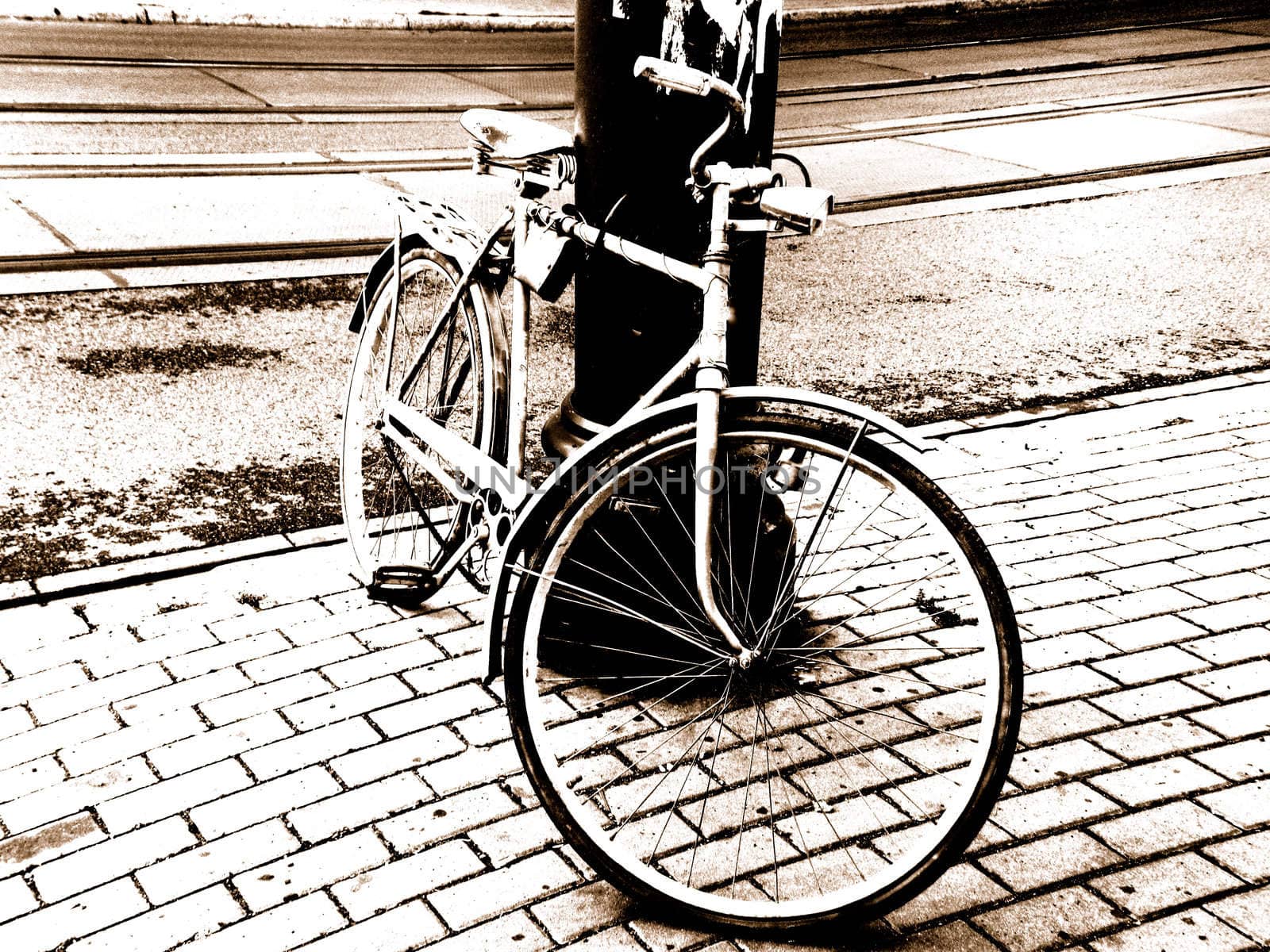 Single bicycle stand in the pavement and  propped against the lamp-post. 