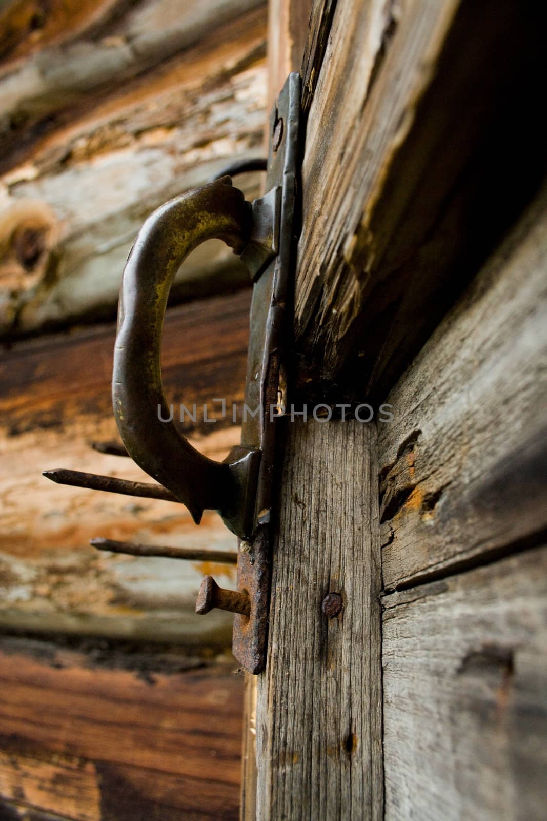 Old rusty doorknob with lots of texture nailed to the cracked wooden 
door.