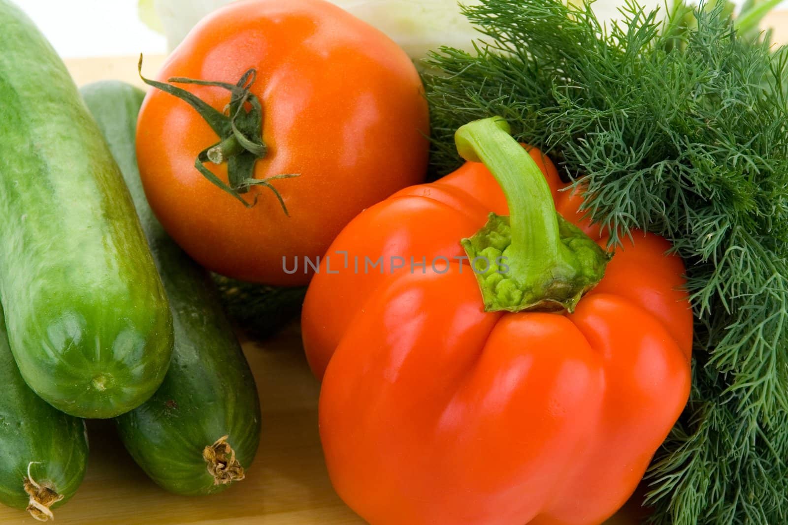 Cucumbers, fennel, tomatoes and bell peppers on a wooden cutting board on a white background