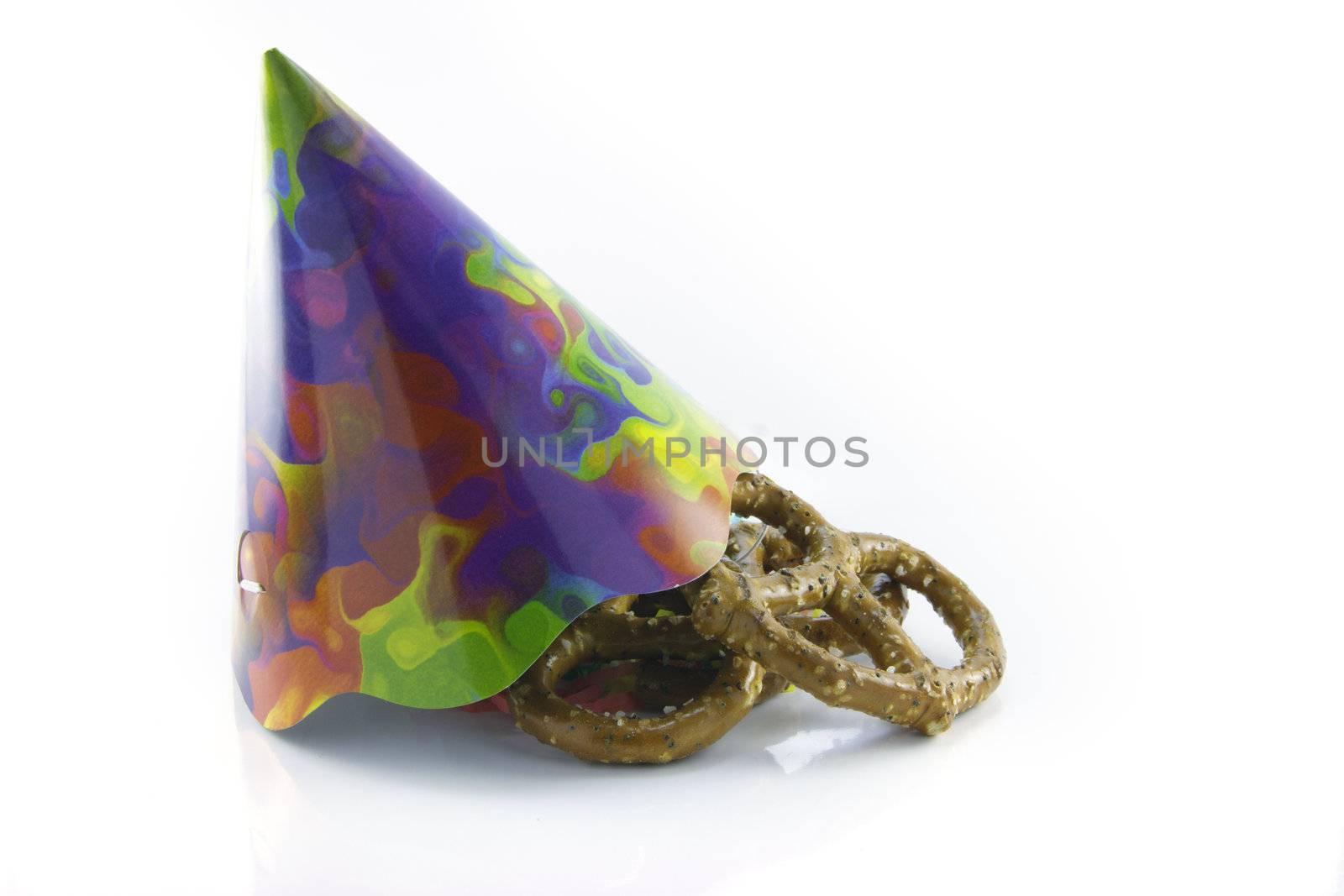 Pile of salty baked pretzels with party hat on a reflective white background