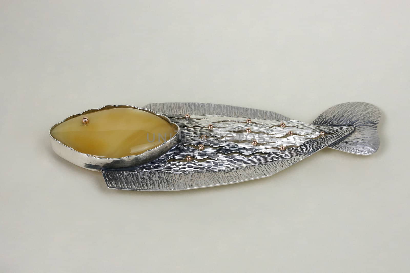 Brooch, made from gold, silver and amber on the light background.
