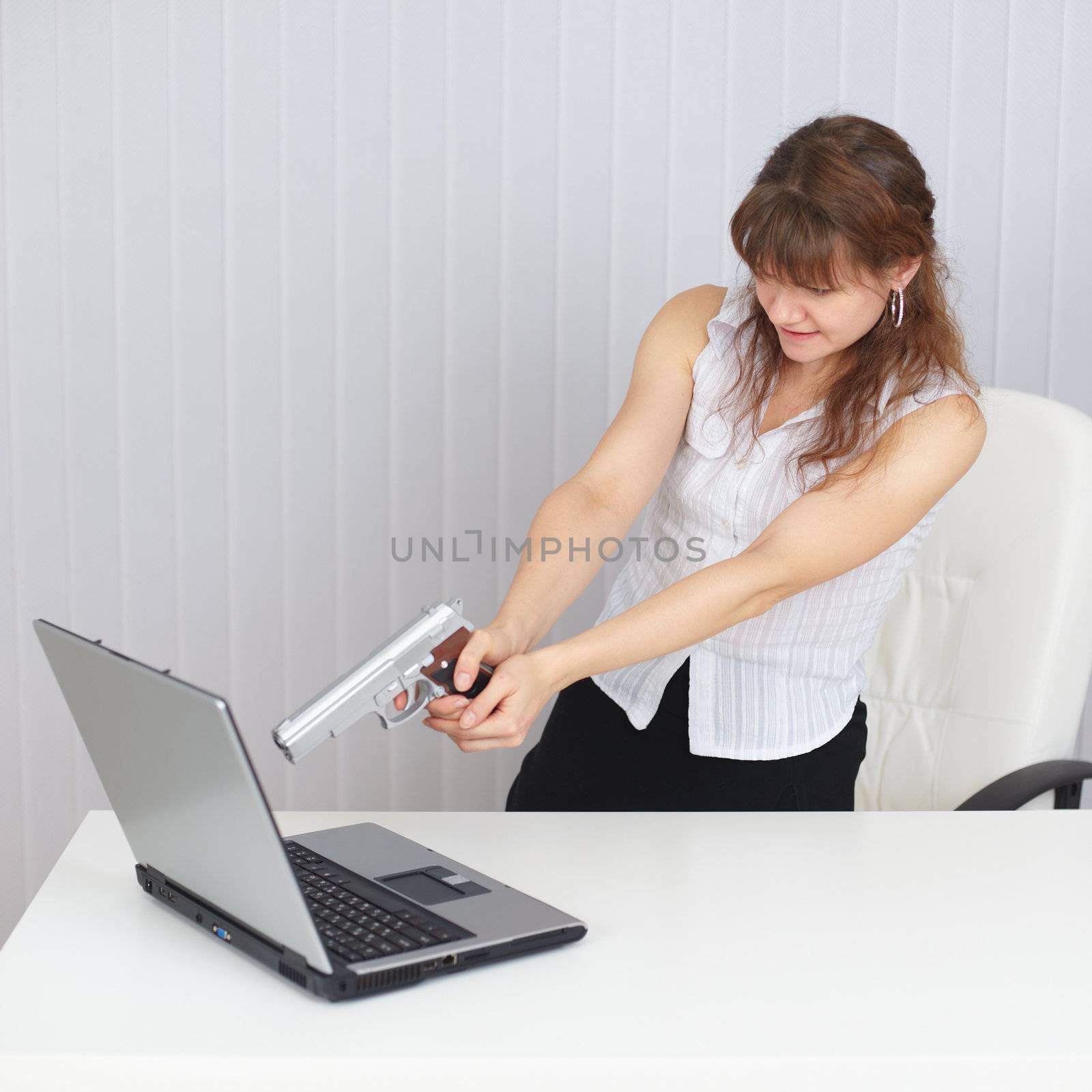 The young woman shoots at the laptop from a pistol