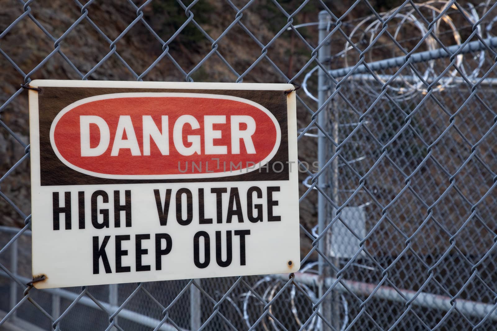 danger, high voltage, keep out -  warning sign on a chain link fence with barbed wire on top protecting hydro power plant