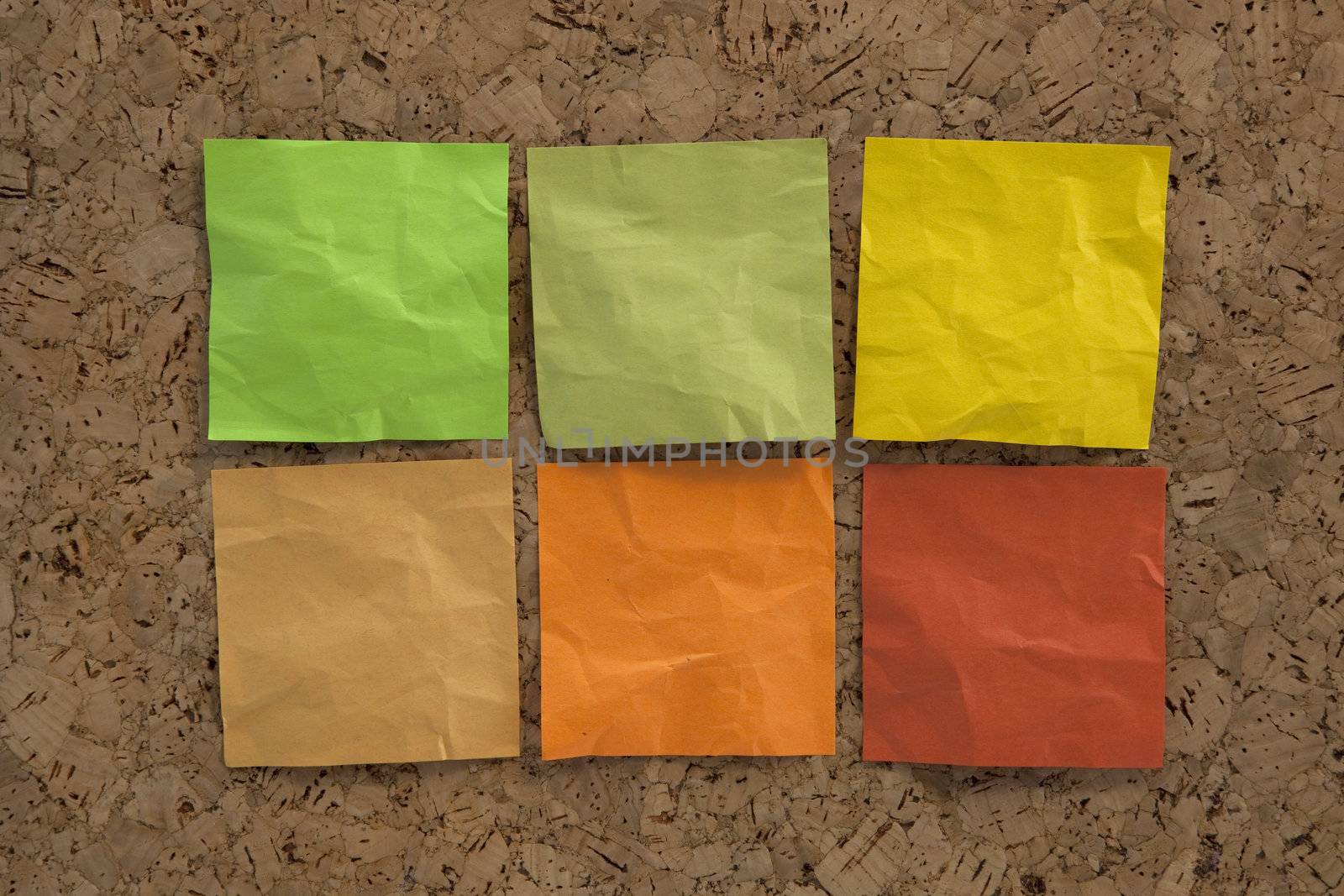 six blank crumpled sticky notes in earth colors (green, brown, yellow) on a cork bulletin board