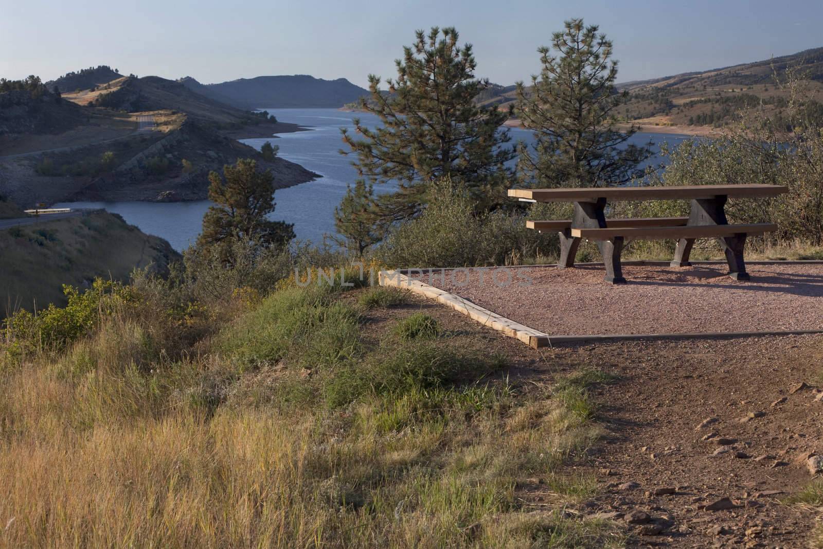 picnic table on shore of mountain reservoir by PixelsAway