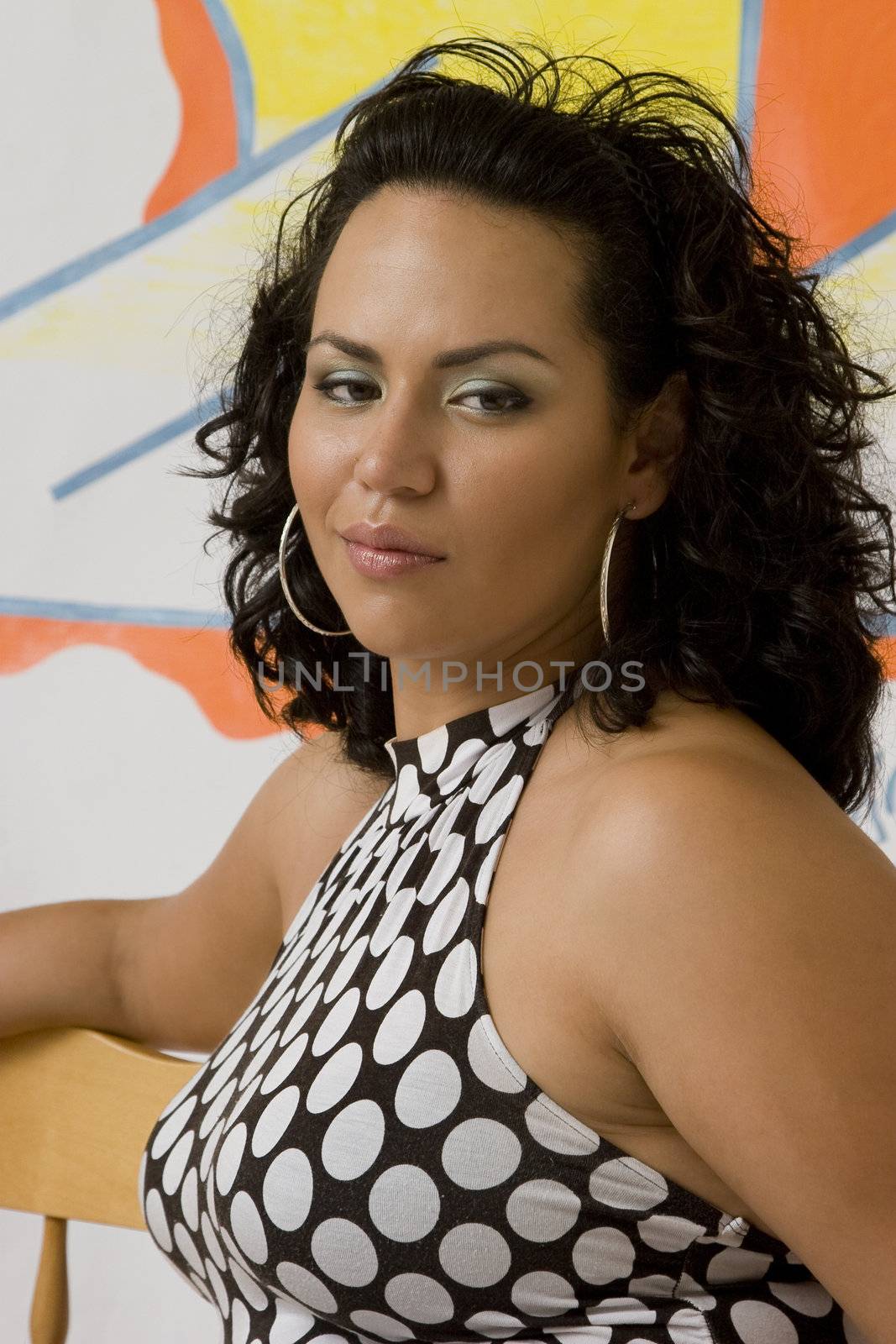 Twenty something latino women sitting on a bench front of a graffiti, with a smirk expression