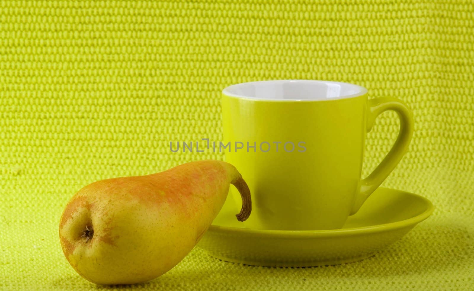 Light green cup on a light green saucer and knife with light green plastic handle on the light green fabric background