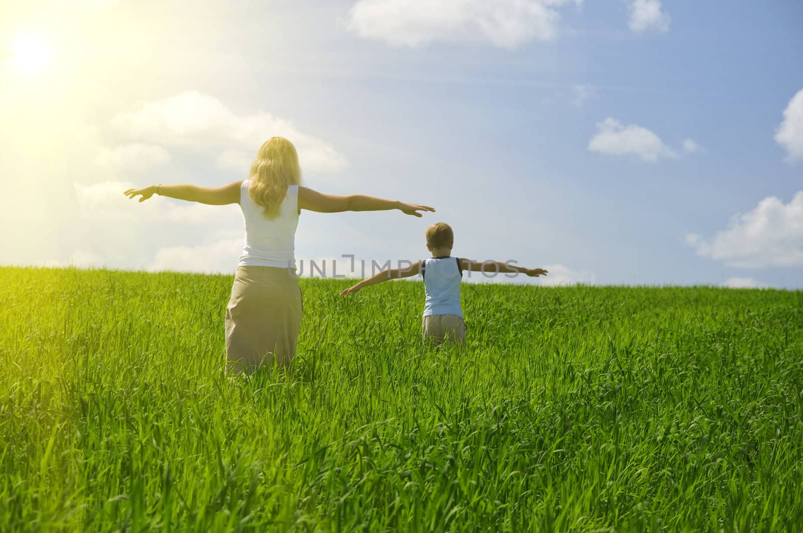ma and son walk in field. agricultural nature landscape with blue cloud sky and green grass