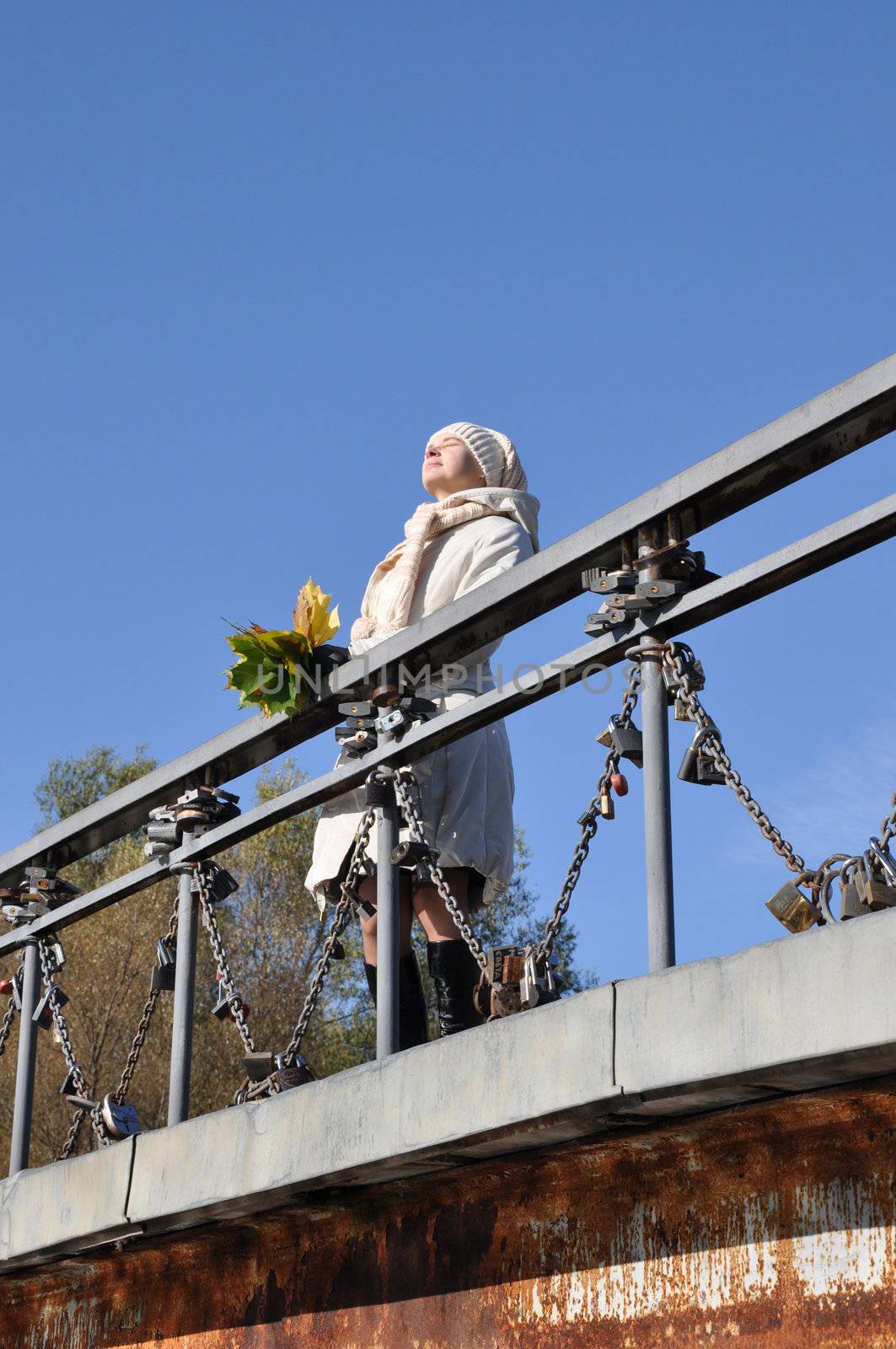 woman sunshines enjoys sunlight on bridge and keeps maple bouquet in hand