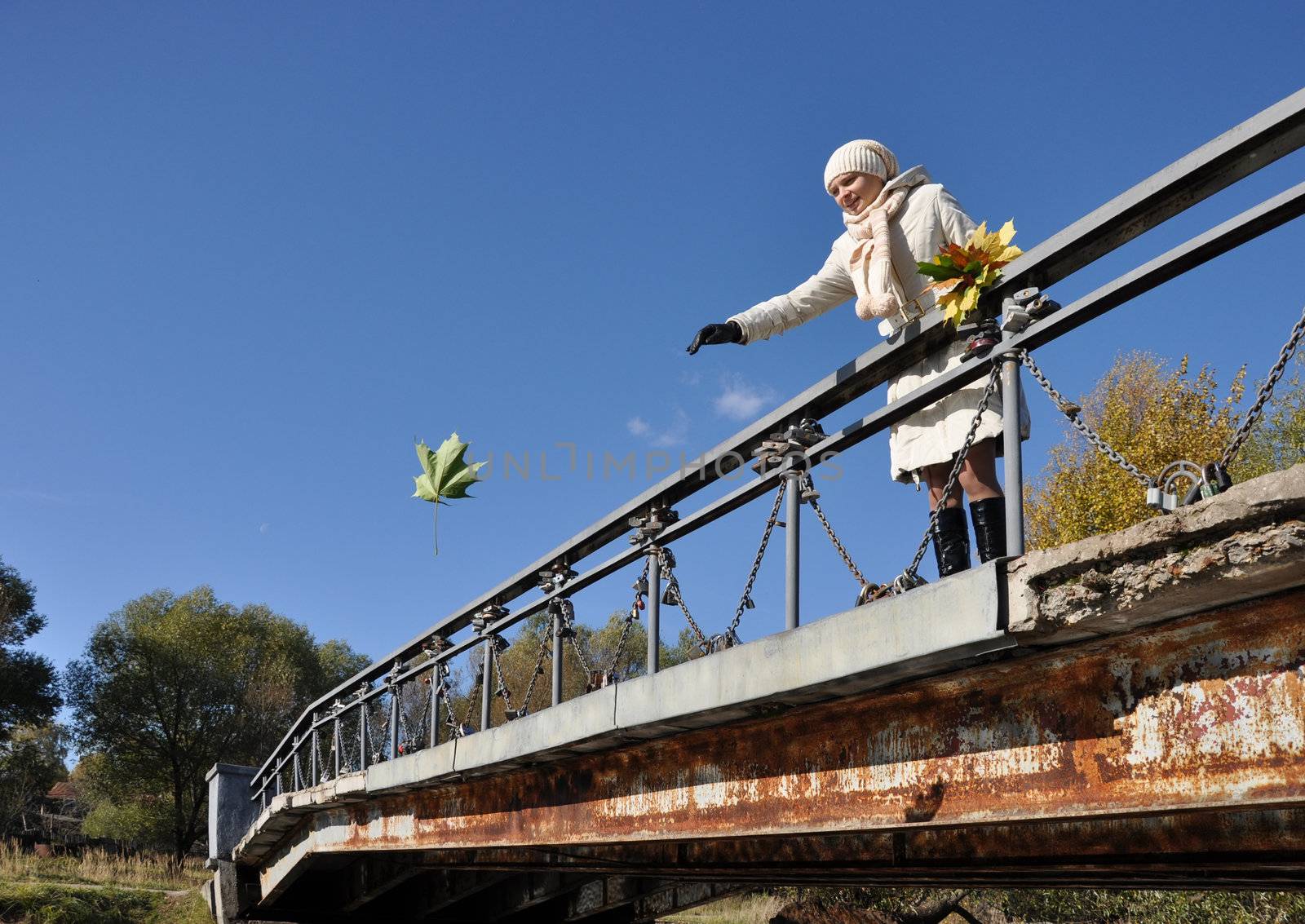 Girl on bridge thinks desire and throws maple leaf in water