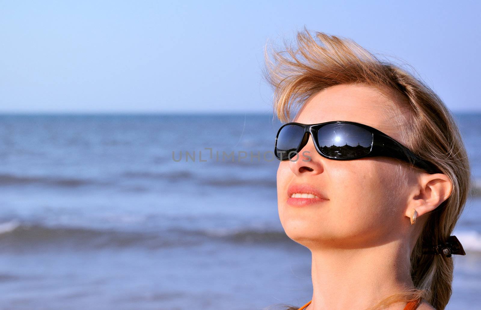 young woman wearing a sunglasses reflecting the beach. sun and an umbrella