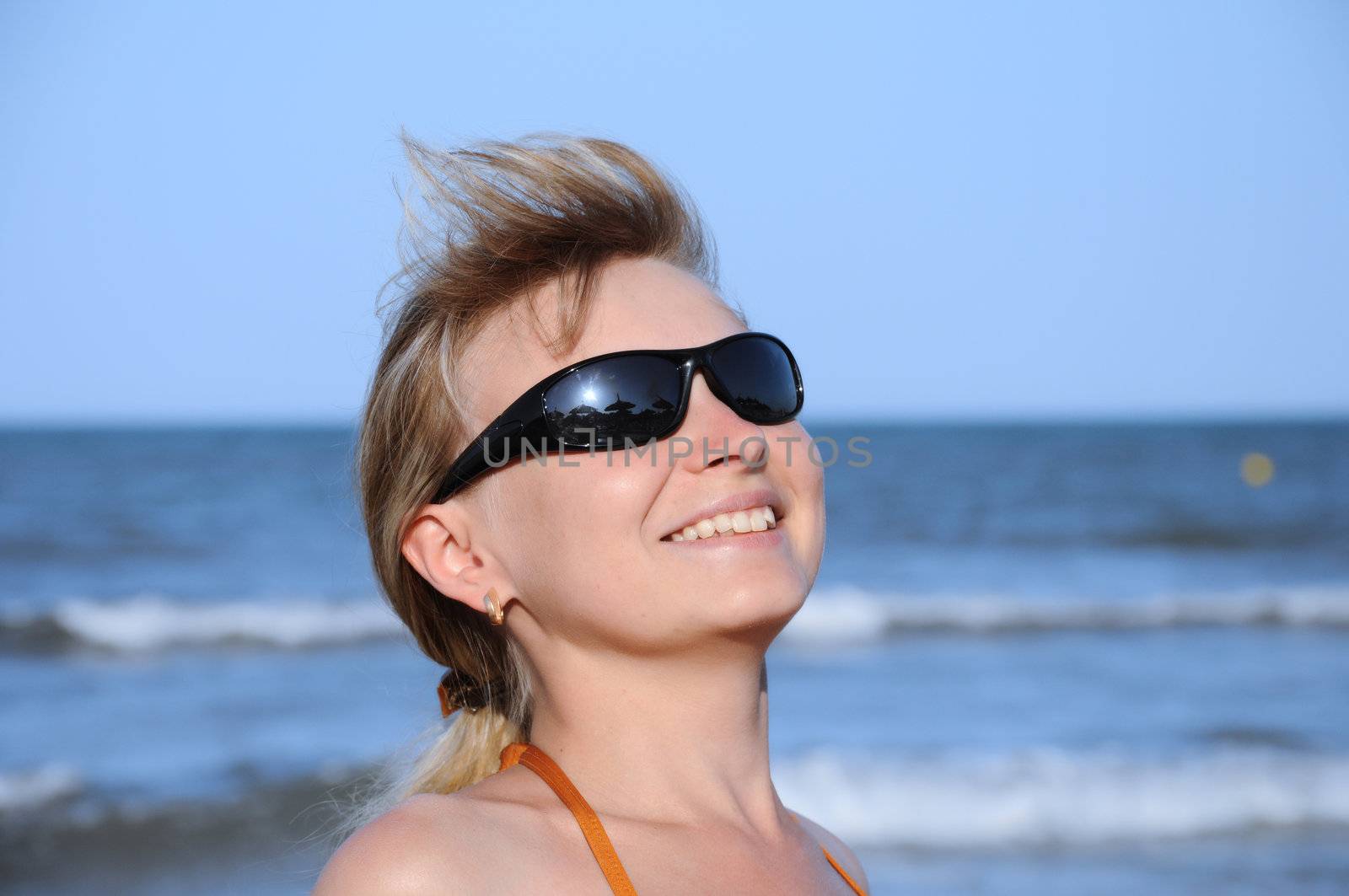 young woman wearing a sunglasses reflecting the beach. sun and an umbrella