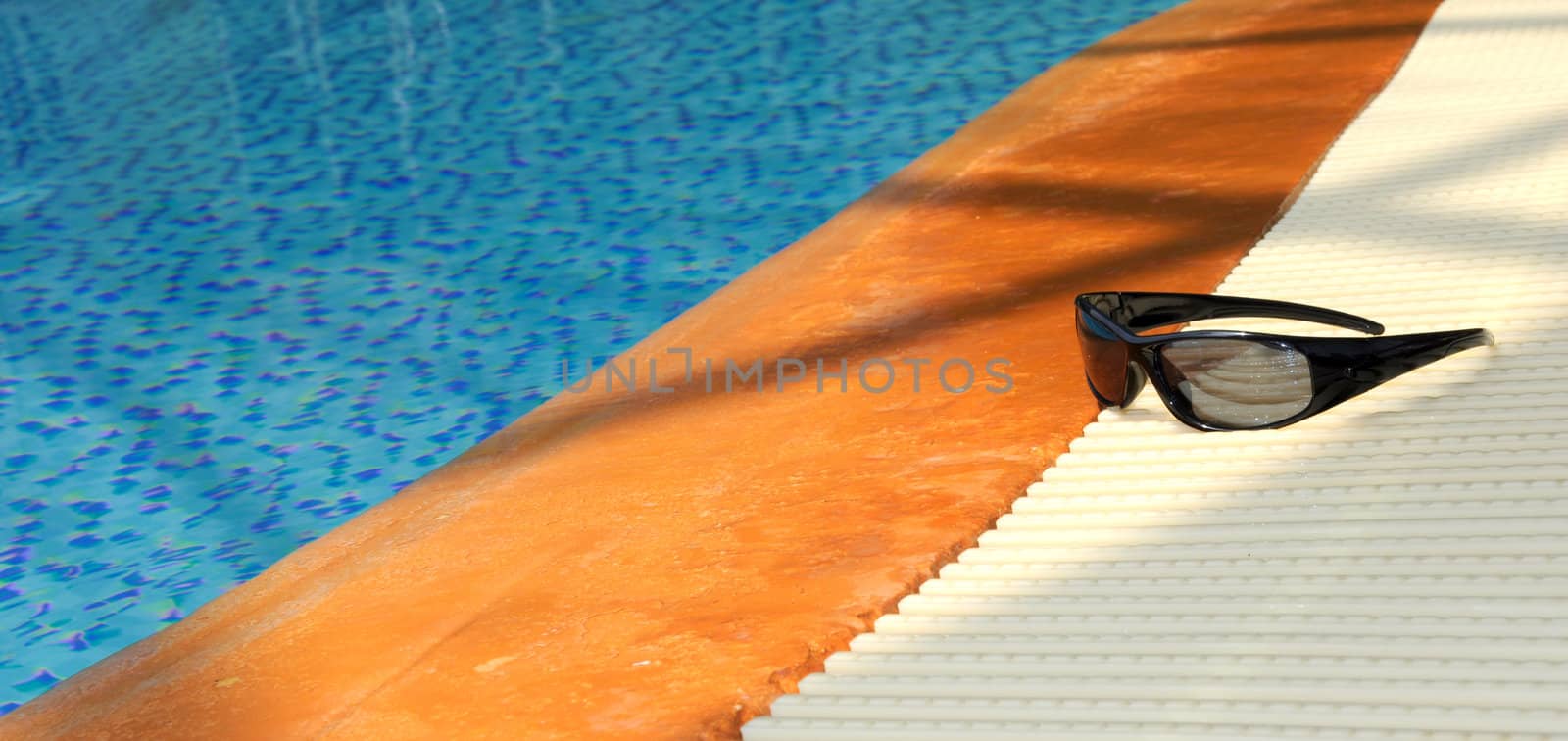 Sunglesses resting on side of a swimming pool: Summer image