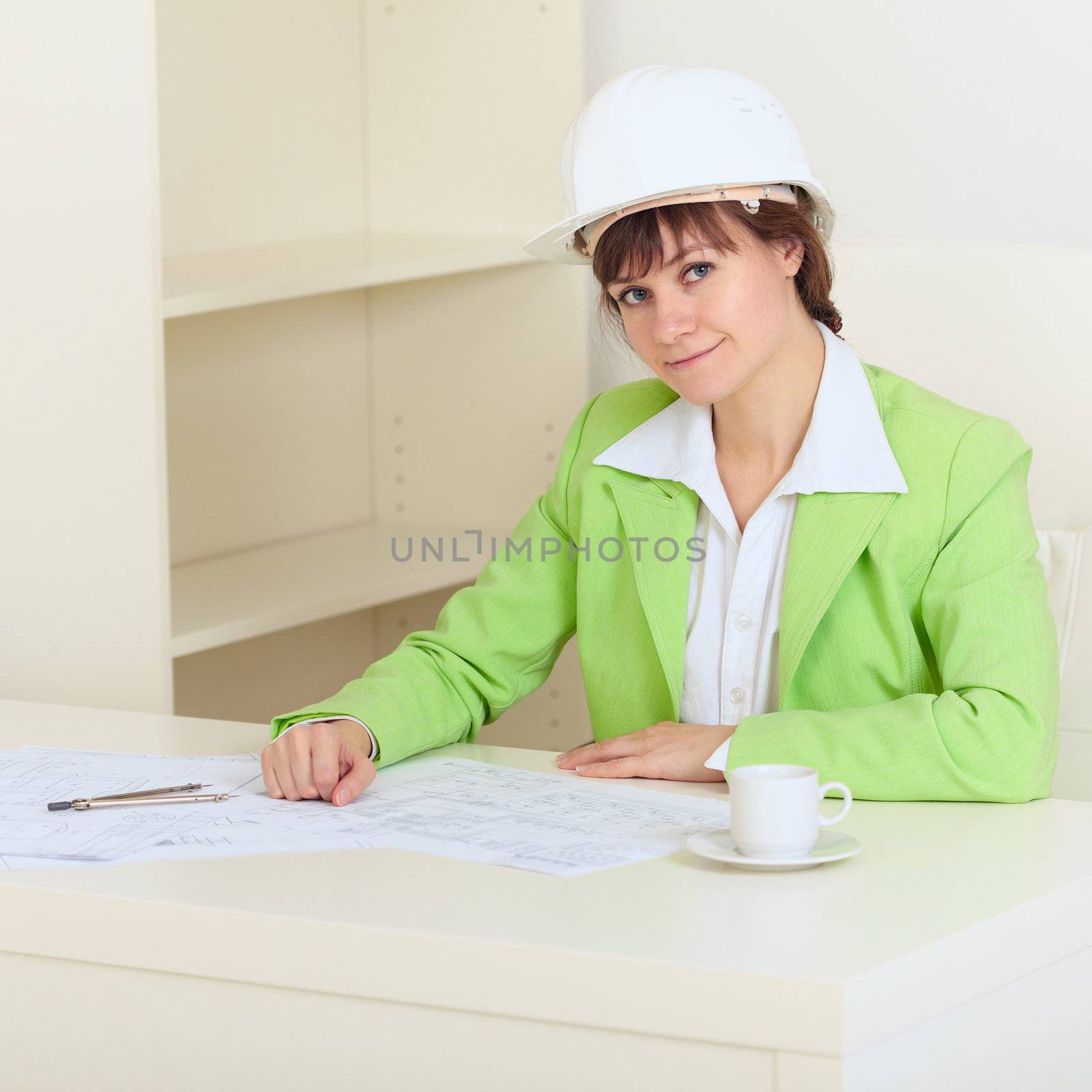 The girl in a protective helmet sits at a table at office