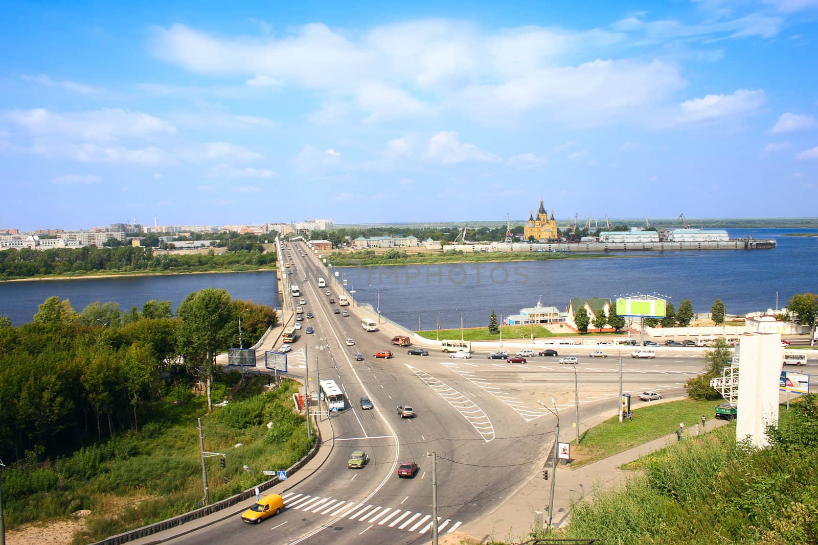 The city bridge through the river with a stream of cars against the blue sky and the river