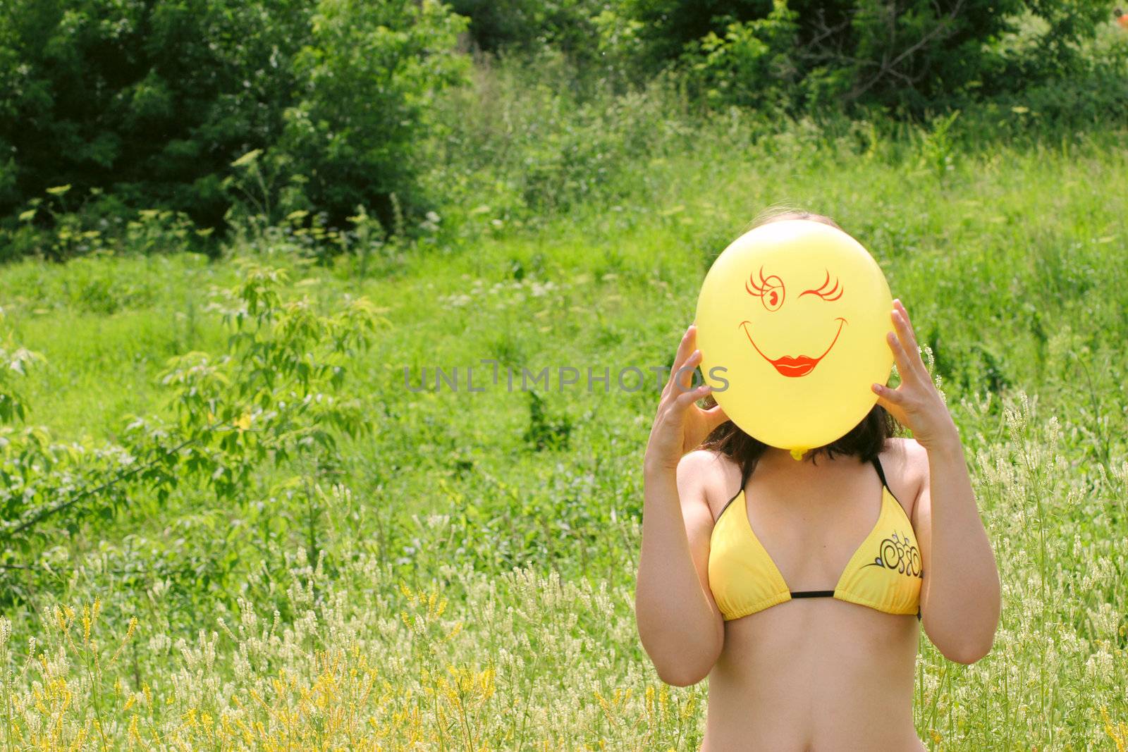 The nice girl in bikini with a yellow balloon removed on a summer field