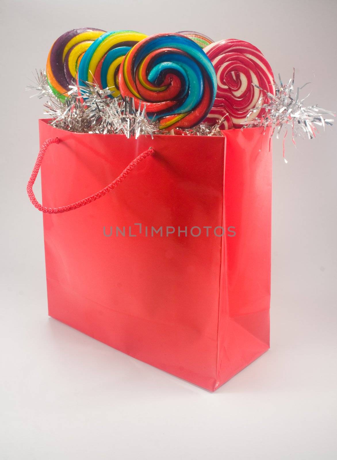 Shiny red gift bag filled with candy against plain background