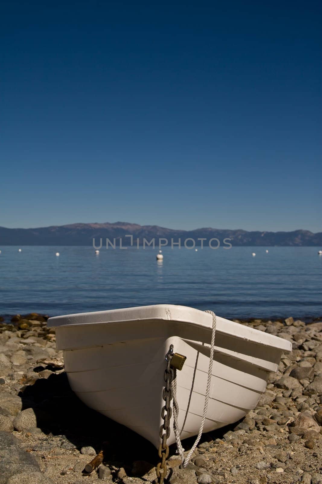 Single plastic boat beached on rocks, lake in background with mountains beyond
