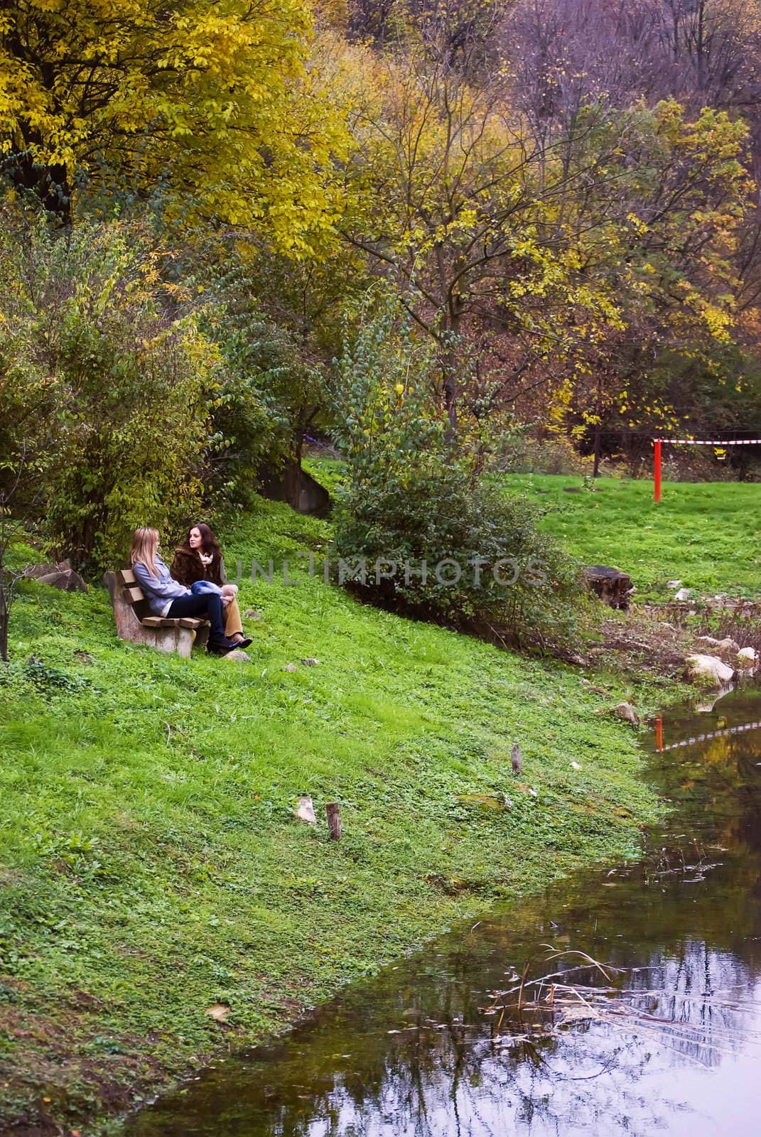 two cute women outdoors in autumn sitting on bench